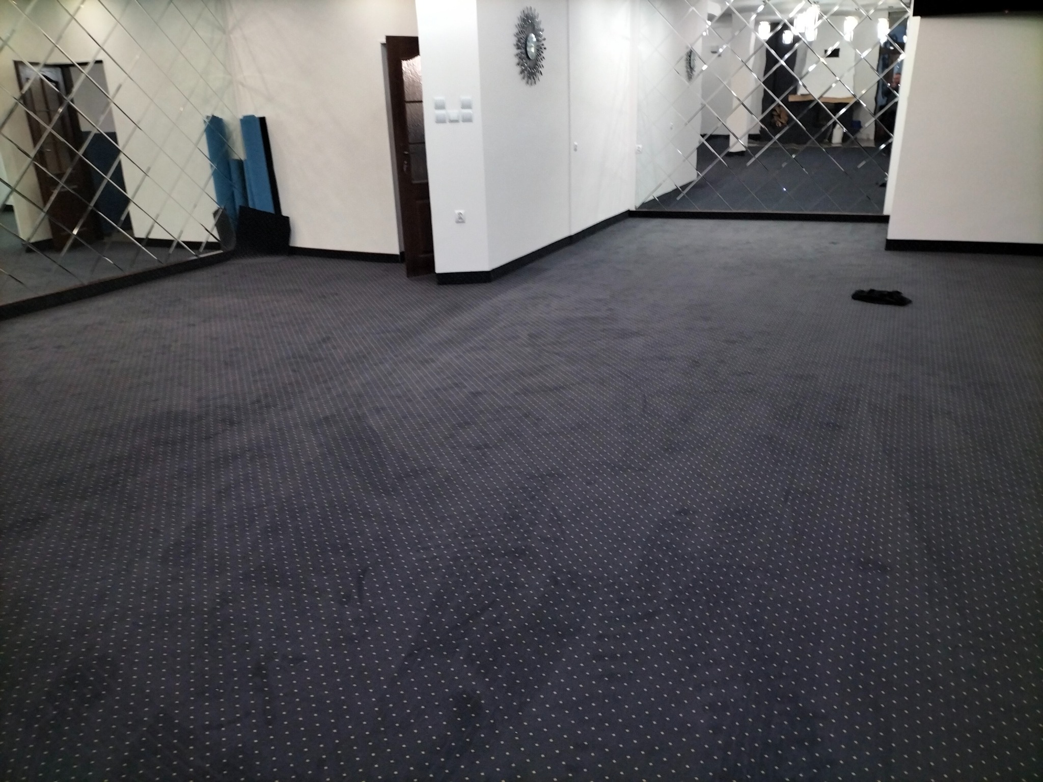 Ciemna wykładzina dywanowa w pokoju z lustrzanymi ścianami i dekoracyjnym zegarem.