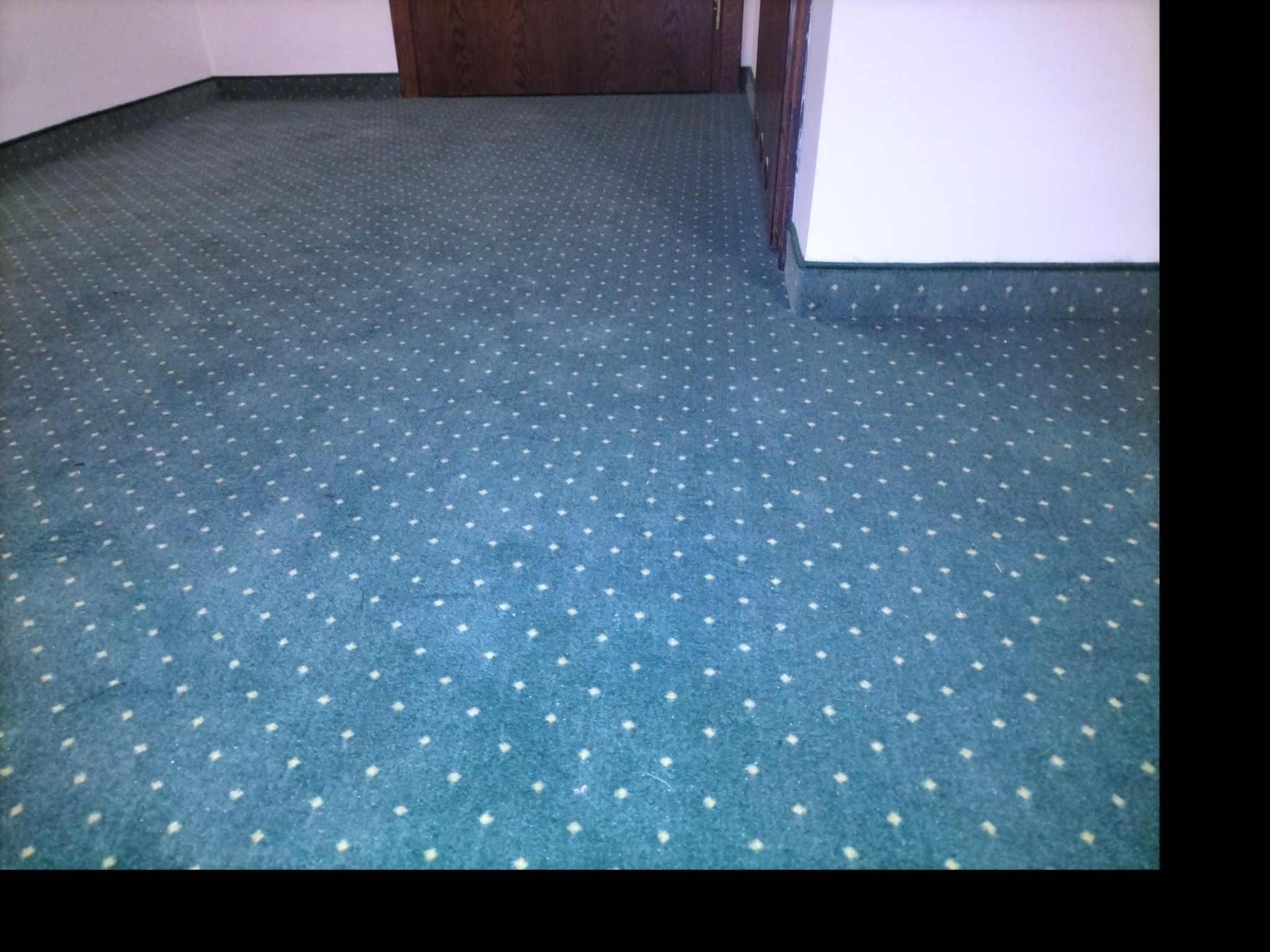 Wykończona podłoga w pokoju z turkusową wykładziną w białe kropki, widoczna listwa przypodłogowa i fragment drzwi. Wykładzina ułożona równo, bez zagnieceń.