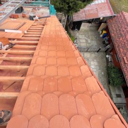 Artur Jasienowicz - Montaż dachówki karpiówki na drewnianej konstrukcji dachu. Widok z góry na częściowo pokryty dach, z narzędziami i elementami więźby dachowej w tle.