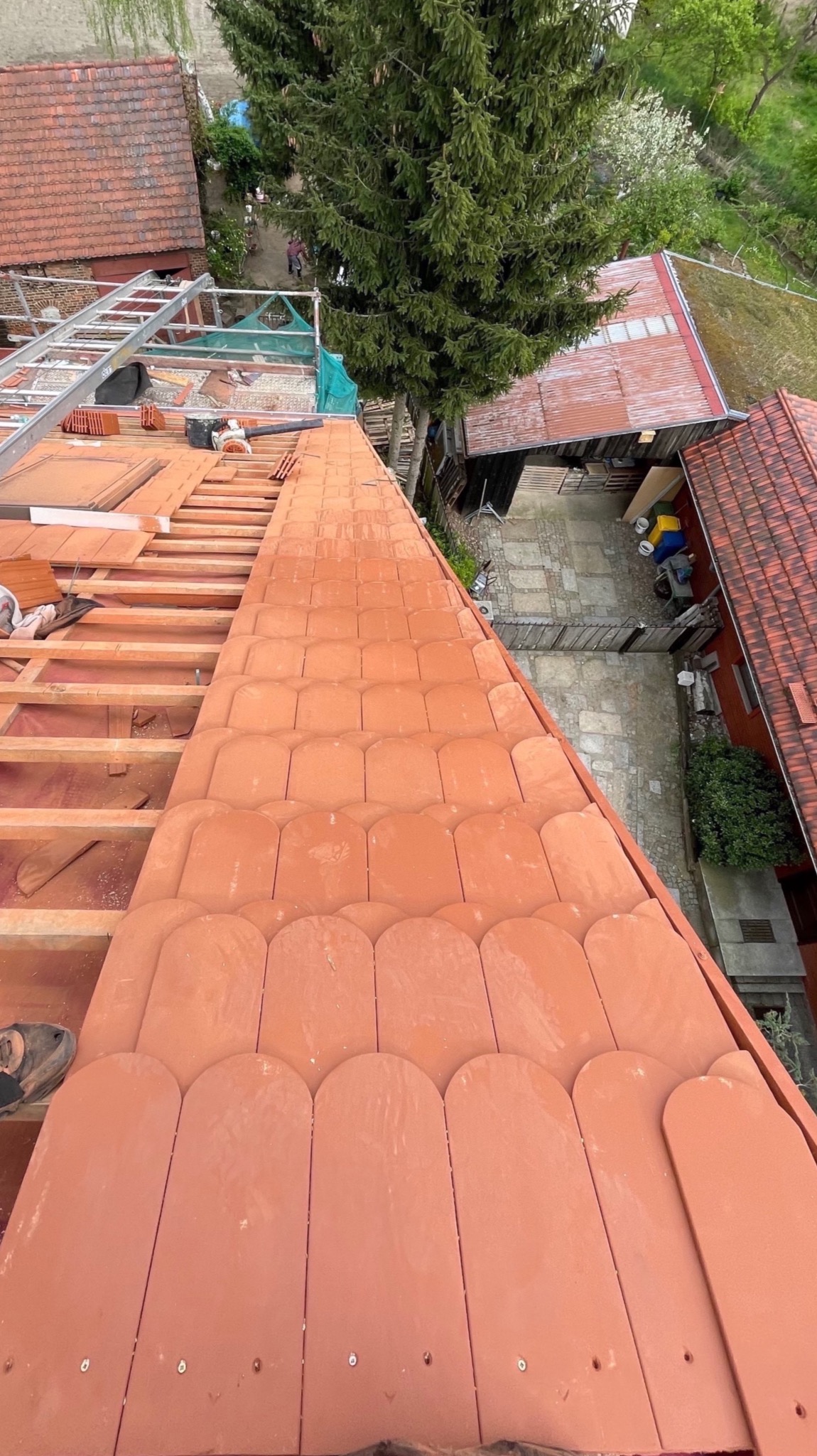 Montaż dachówki karpiówki na drewnianej konstrukcji dachu. Widok z góry na częściowo pokryty dach, z narzędziami i elementami więźby dachowej w tle.