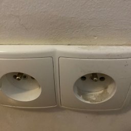 Magiczny blysk - Dwa białe, brudne gniazdka elektryczne na ścianie, widoczne ślady użytkowania i zabrudzenia wokół otworów.
