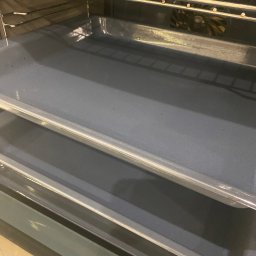 Magiczny blysk - Wnętrze czystego piekarnika z metalowymi półkami i wentylatorem w tle, ukazane z bliska pod kątem, prezentujące efekt sprzątania.