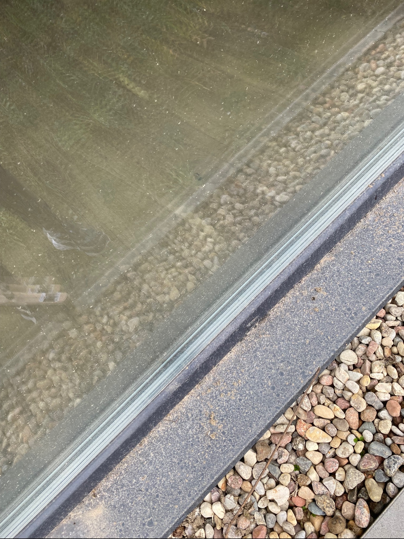 Brudna szyba okna z widocznymi smugami i zaciekami, otoczona kamieniami dekoracyjnymi.