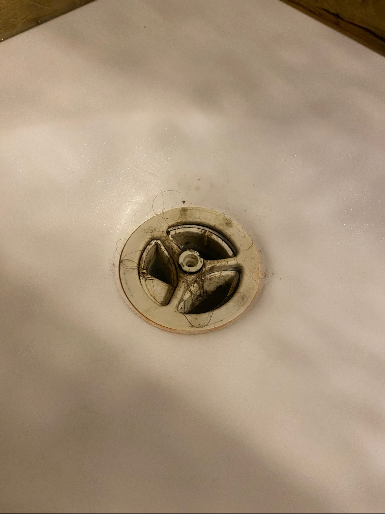 Zablokowany odpływ w białej wannie, widoczne włosy i zabrudzenia wokół metalowego sitka.