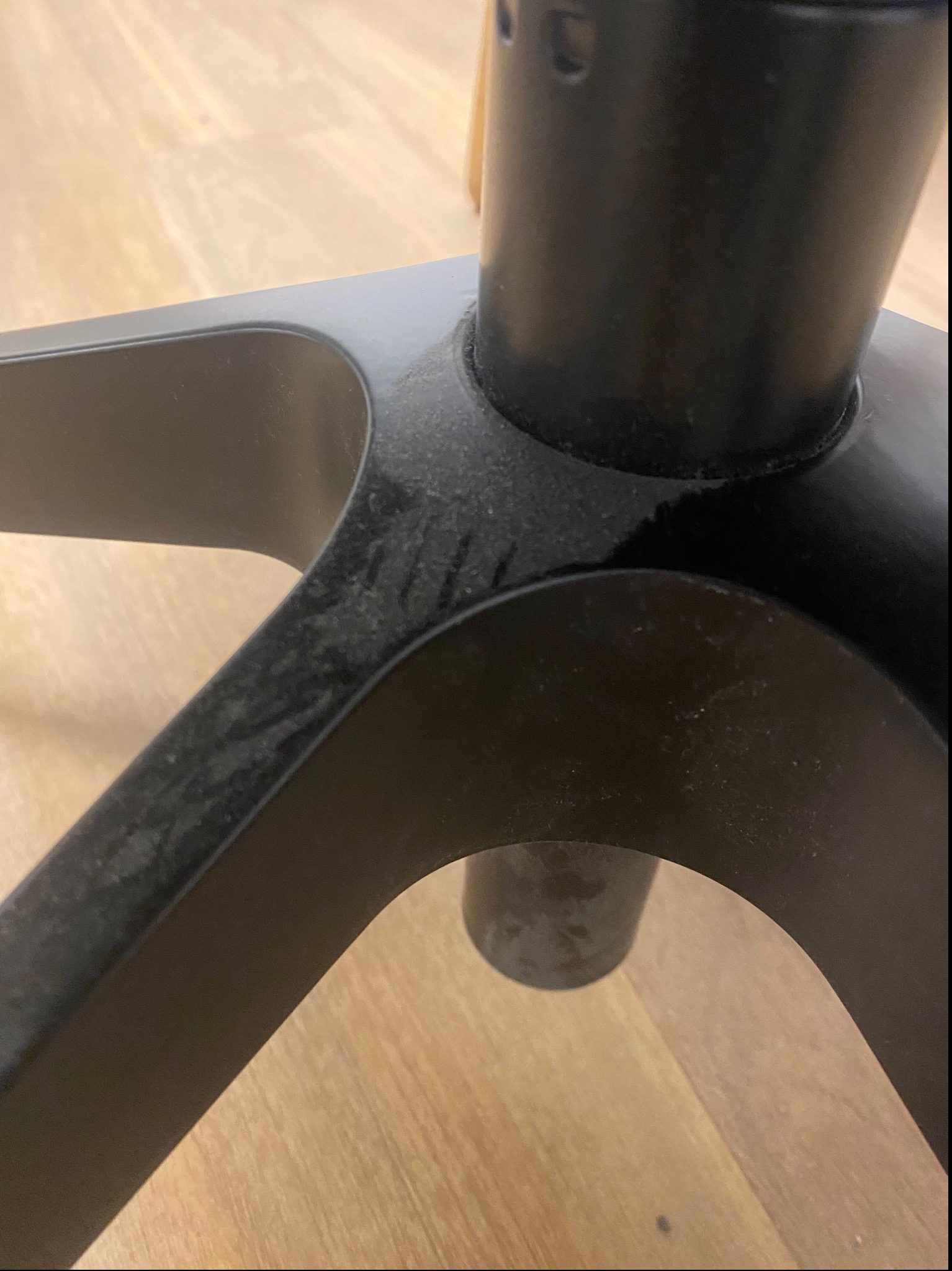 Niski kąt: Podstawa czarnego krzesła biurowego z widocznym kurzem na drewnianej podłodze. Detal prezentujący zaniedbanie przed sprzątaniem.