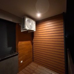 LESKI-KLIM - Klimatyzator zamontowany na drewnianej ścianie w Mielcu, widoczne drewniane deski podłogowe i ciemne otoczenie.