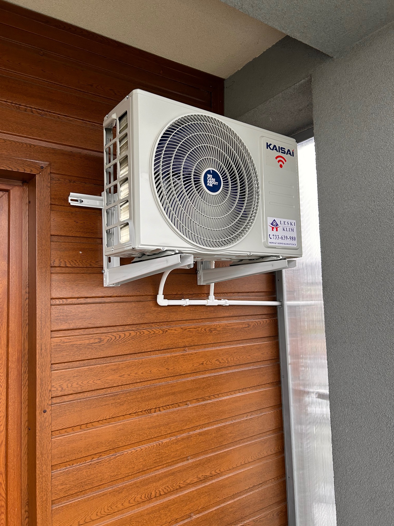 Zewnętrzna jednostka klimatyzacji Kaisai zamontowana na drewnianej elewacji domu, widoczna instalacja odprowadzająca skropliny i naklejka firmy serwisowej Leski Klim.