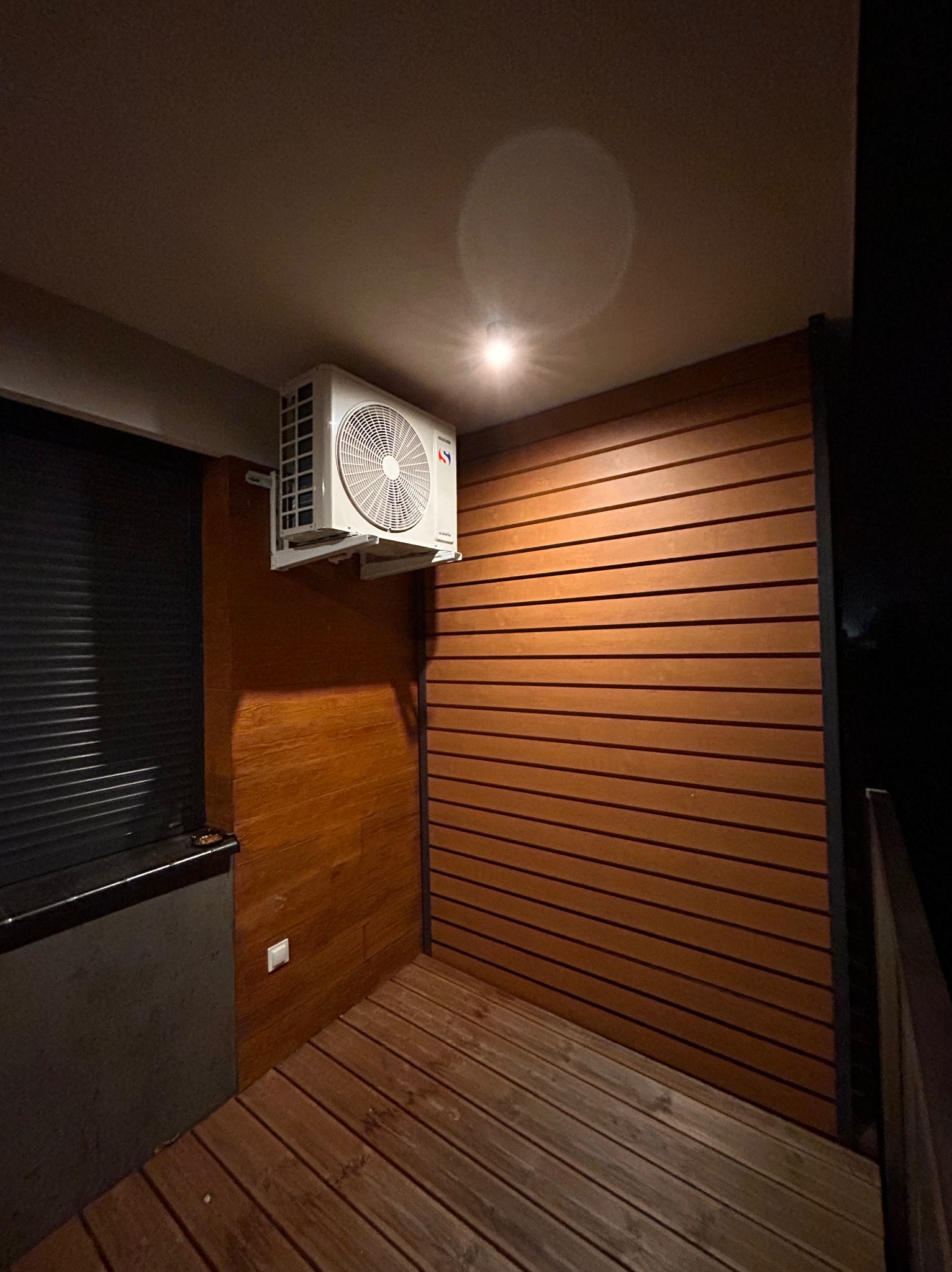 Klimatyzator zamontowany na drewnianej ścianie w Mielcu, widoczne drewniane deski podłogowe i ciemne otoczenie.