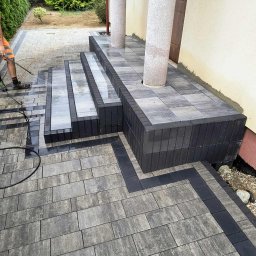 Błażej Łabędzki - Umyte schody z kostki brukowej prowadzące do domu z kolumnami, widoczne świeże fugi i mokra powierzchnia, czyszczone przez osobę w pomarańczowych spodenkach.