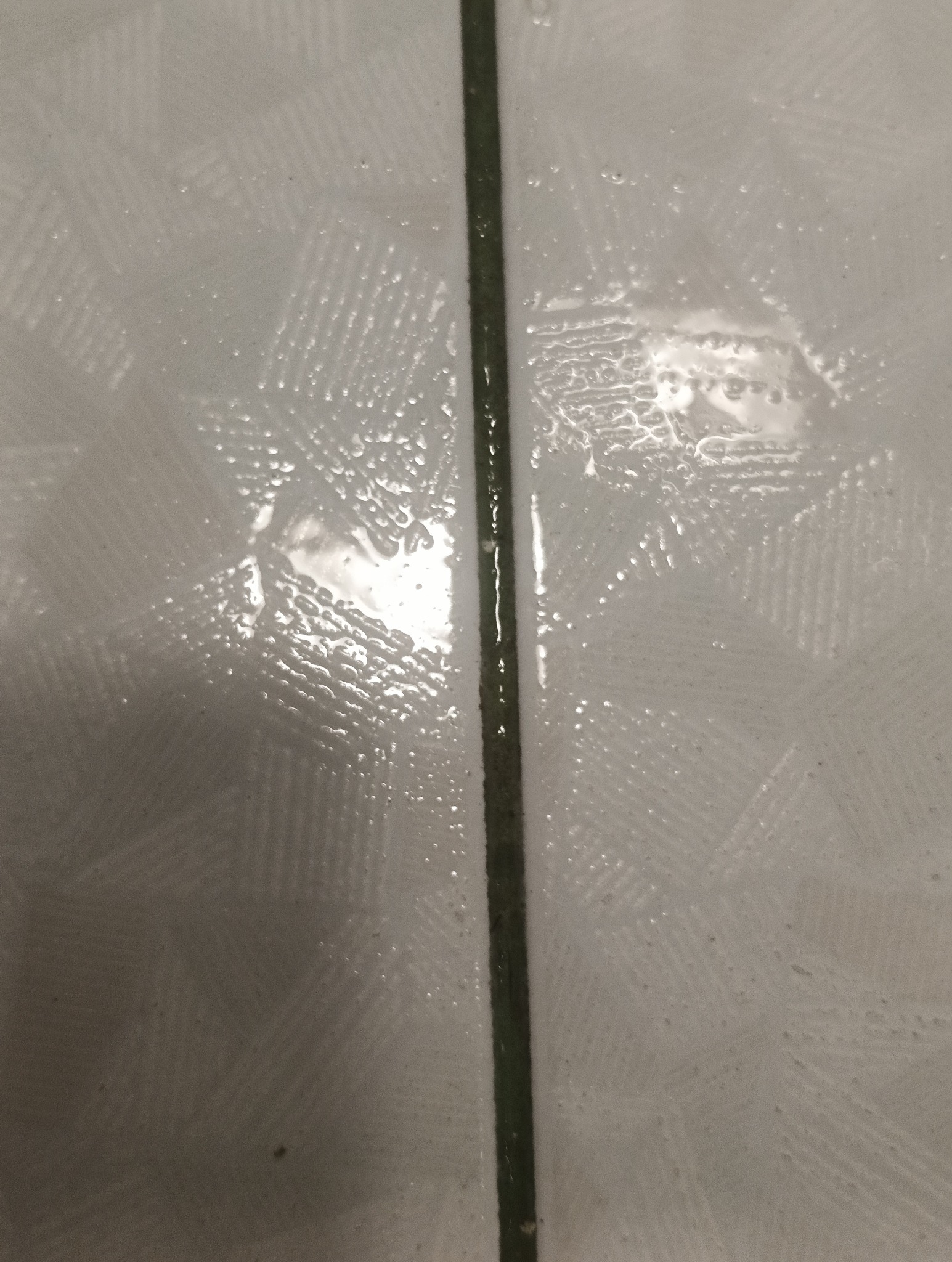 Zbliżenie na mokre, białe płytki z ciemną fugą, pokryte kroplami wody po czyszczeniu.