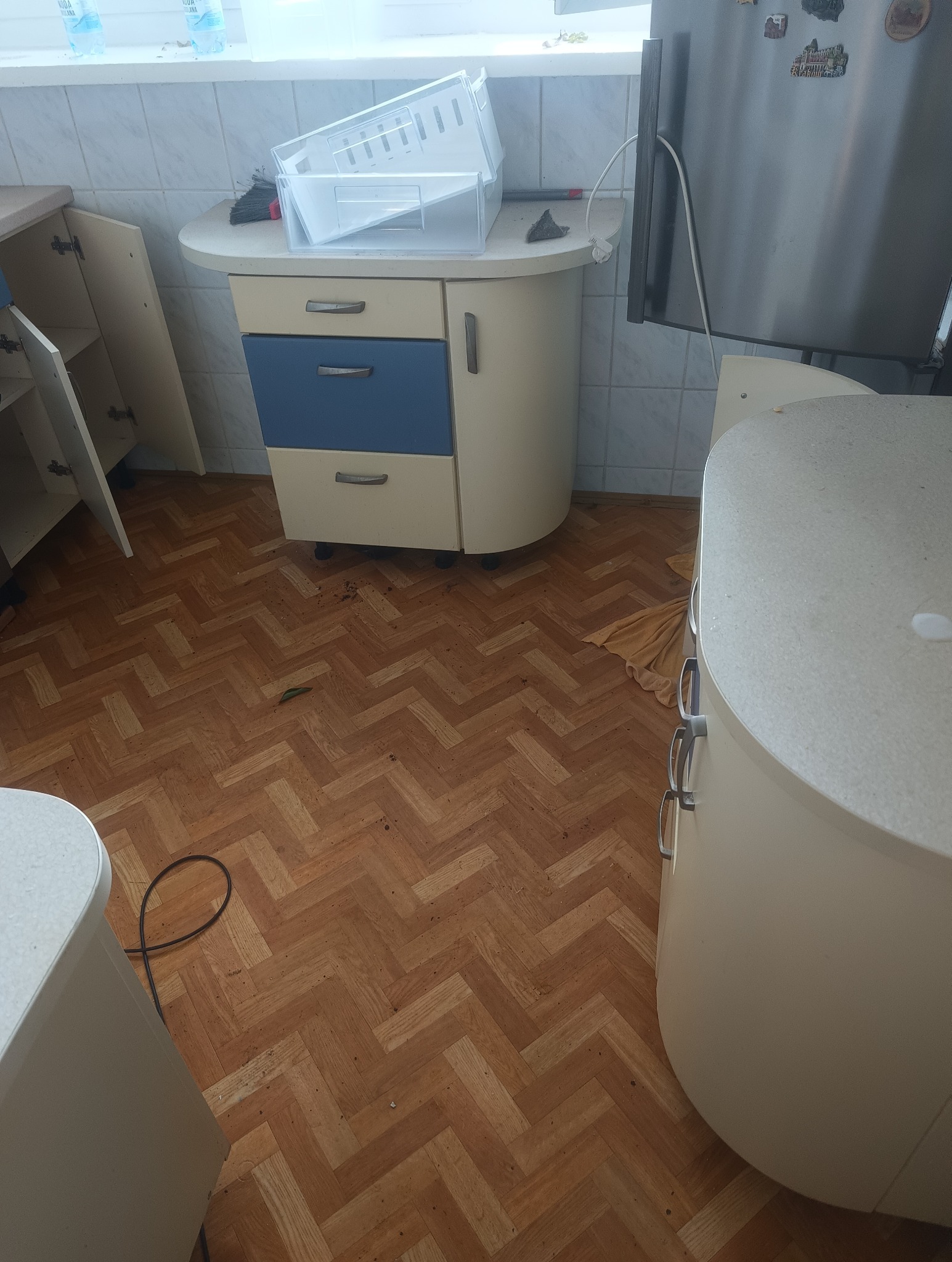 Kuchnia w trakcie opróżniania: otwarte szafki, wysunięte szuflady, drobne zabrudzenia na parkiecie ułożonym w jodełkę, widoczne pojemniki plastikowe na blacie.