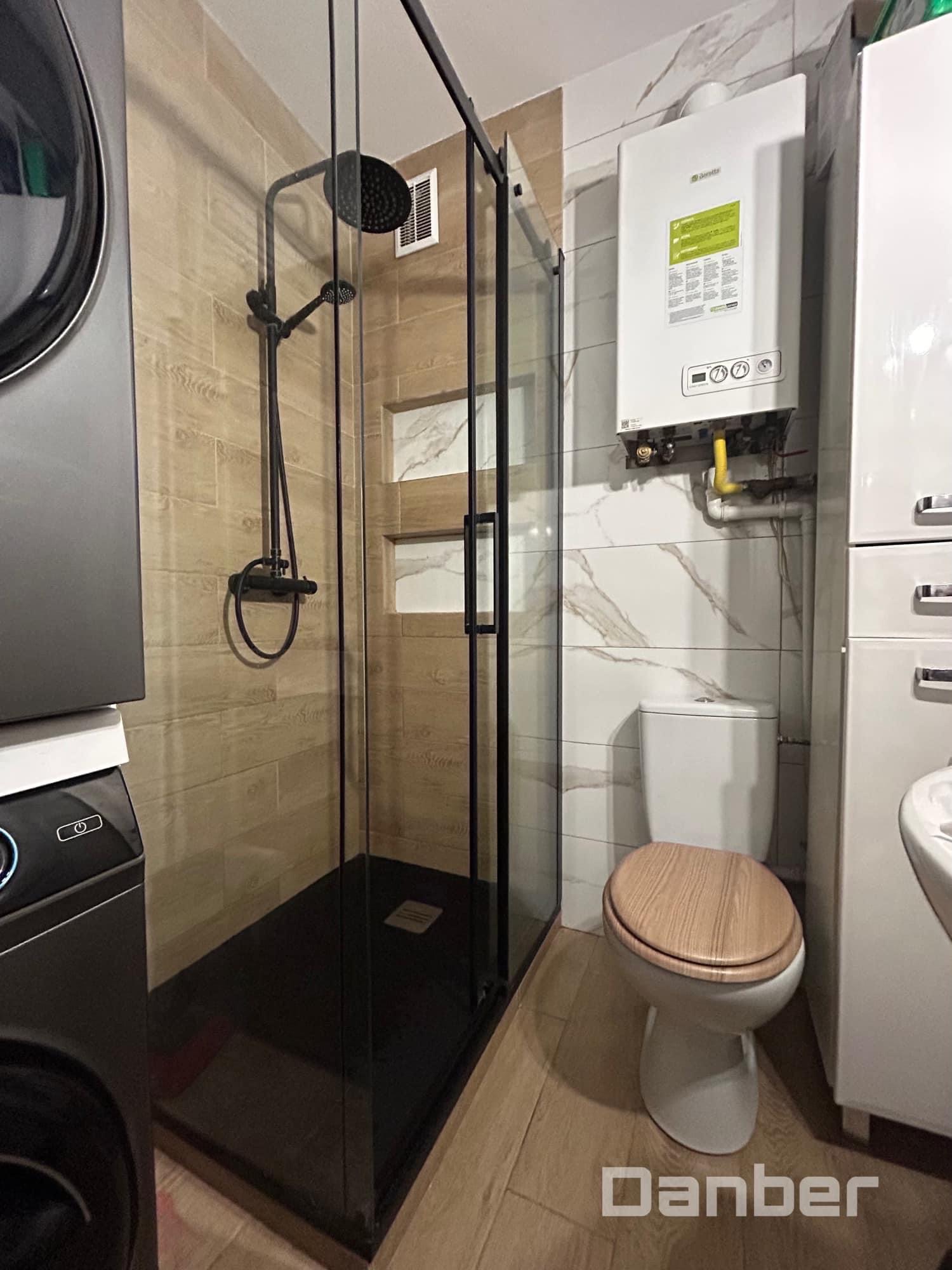 Nowoczesna łazienka z kabiną prysznicową typu walk-in z czarnym wykończeniem, drewnopodobnymi płytkami na ścianie, wiszącym piecem gazowym i toaletą z drewnianą deską.