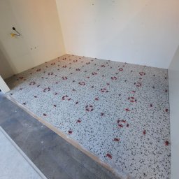 Mykhailo Lavryshyn V&M Construction - W trakcie układania jasnoszarej terazzo podłogi, widoczne czerwone klipsy poziomujące, ściany przygotowane pod malowanie.