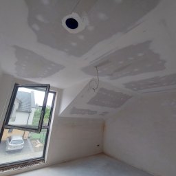 Mykhailo Lavryshyn V&M Construction - Poddasze w trakcie szpachlowania: widoczne fragmenty płyt kartonowo-gipsowych na skośnym suficie, okno dachowe z widokiem na dom i samochód. Przygotowanie do malowania.