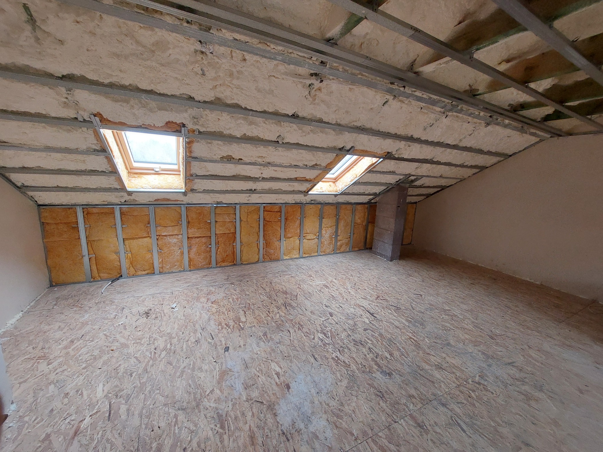 Poddasze w trakcie izolacji: widoczne metalowe profile, wełna mineralna, okna dachowe i płyta OSB na podłodze. Etap prac wykończeniowych.