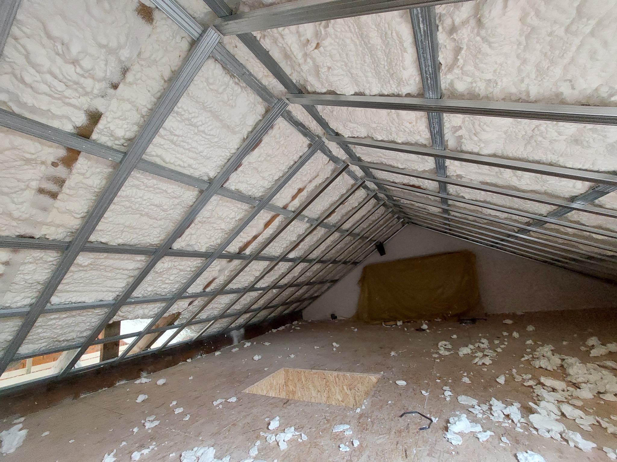 Izolacja poddasza pianą PUR i metalowa konstrukcja stelaża pod płyty G-K, widok z dołu. Otwór w podłodze i resztki piany.