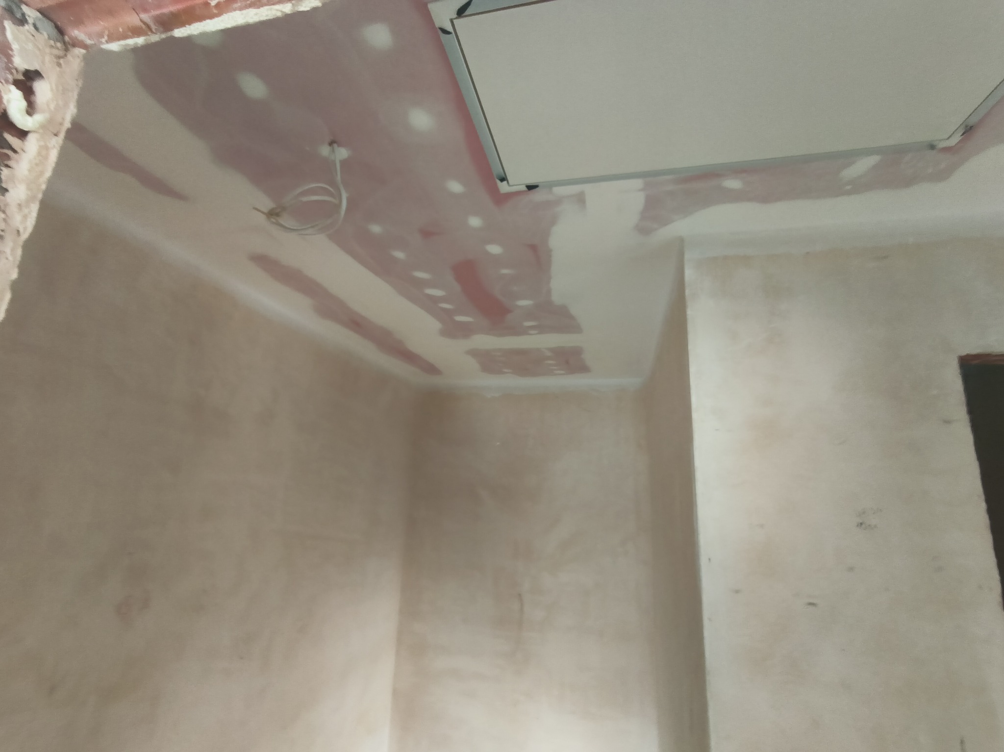 Wnętrze w trakcie szpachlowania: sufit z widocznymi łatami szpachli, fragment instalacji elektrycznej i klapa rewizyjna. Ściany przygotowane do dalszych prac wykończeniowych.