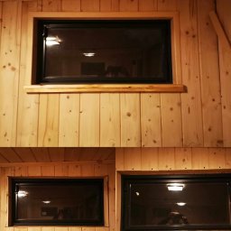 GK Gabriel Kukułowicz - Wnętrze wykończone boazerią z widocznymi dwoma oknami z czarnymi ramami; w szybach okiennych odbija się oświetlenie i sylwetka osoby robiącej zdjęcie.