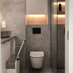 GK Gabriel Kukułowicz - Nowoczesna łazienka z szarą płytką, podświetlanymi szafkami i umywalką z szufladą na pranie. Minimalistyczny design z czarnymi akcentami i szklanym panelem prysznicowym.