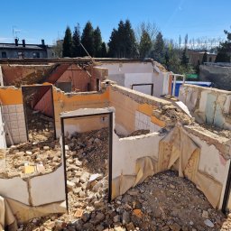 ZLK Multi Biznes Company Łukasz Zieliński - Wnętrze zrujnowanego domu z resztkami tapet i gruzem, widok na zewnątrz, gdzie stoi mężczyzna i widać drzewa.