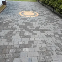 Niejednolicie wyczyszczona kostka brukowa z dekoracyjnym, okrągłym wzorem z żółtej kostki. Widoczne różnice w czystości kostki.