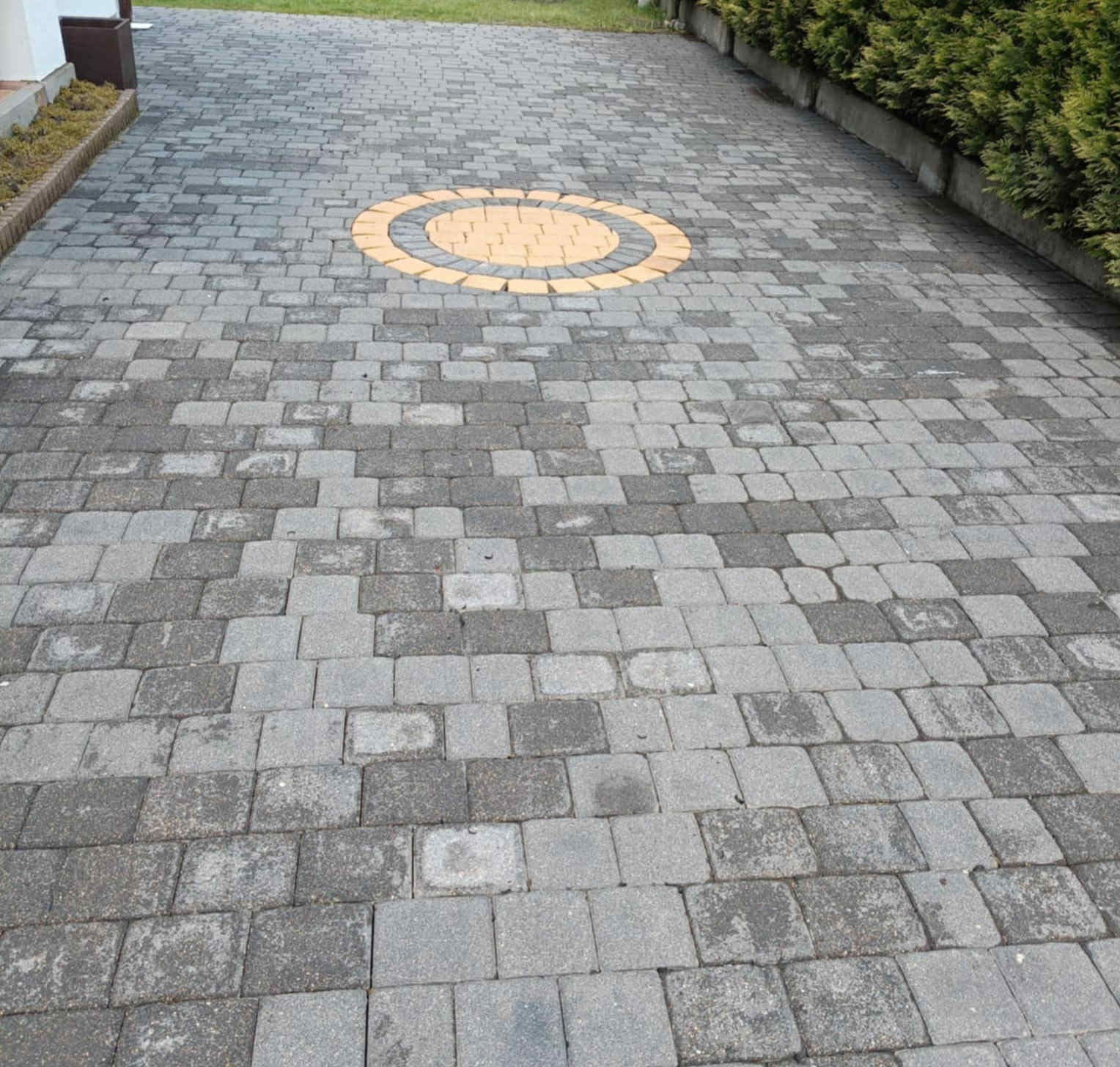 Niejednolicie wyczyszczona kostka brukowa z dekoracyjnym, okrągłym wzorem z żółtej kostki. Widoczne różnice w czystości kostki.