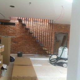 Albert Brzezin - Wnętrze w trakcie prac wykończeniowych: surowa ceglana ściana z metalowymi schodami, widoczne kartony, narzędzia i odkurzacz przemysłowy Festool.