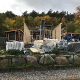 Albert Brzezin - Budowa szkieletowej konstrukcji domu z widocznymi elementami drewnianymi, rusztowaniami i materiałami budowlanymi na tle jesiennego krajobrazu.