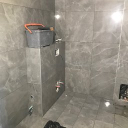 Albert Brzezin - Łazienka w trakcie wykończenia w Radomiu: szare, marmurowe płytki na ścianach i podłodze, widoczne narzędzia glazurnicze i instalacje. Prace wykończeniowe.