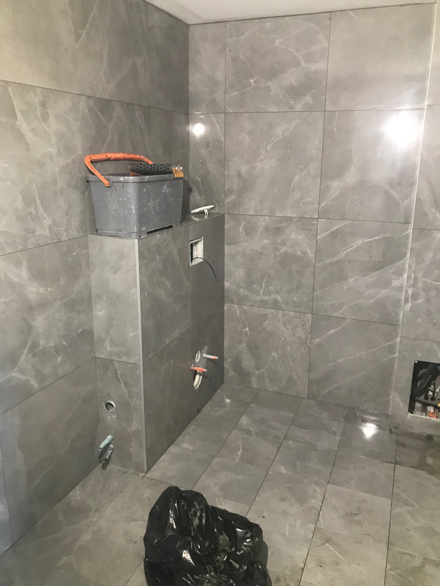 Łazienka w trakcie wykończenia w Radomiu: szare, marmurowe płytki na ścianach i podłodze, widoczne narzędzia glazurnicze i instalacje. Prace wykończeniowe.