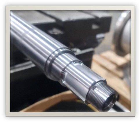 Precyzyjnie obrobiony, metalowy wał z gwintem na końcu, widoczne ślady po obróbce skrawaniem, umieszczony na tle warsztatowym.