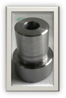 Metalowy element cylindryczny z otworem, widoczne ślady obróbki, szlifowana powierzchnia, ułożony na szarej powierzchni.