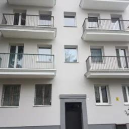 Elewacja budynku po renowacji z balkonami o różnych balustradach i odnowioną strefą wejścia z ciemnymi drzwiami i szarą lamperią.