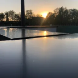 Błyszcząca powierzchnia dachu odbija zachodzące słońce, tworząc złote refleksy na tle drzew.