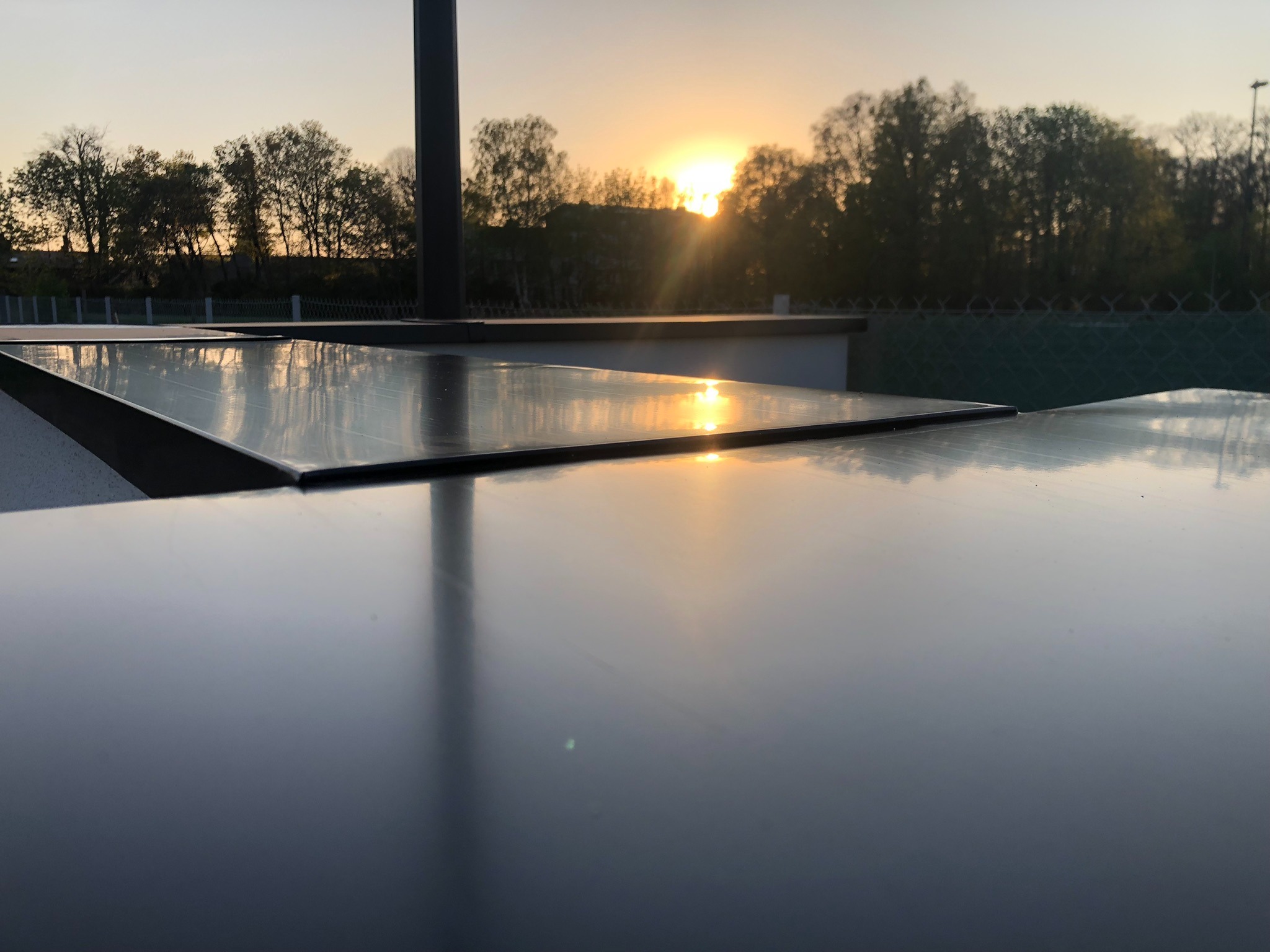 Błyszcząca powierzchnia dachu odbija zachodzące słońce, tworząc złote refleksy na tle drzew.