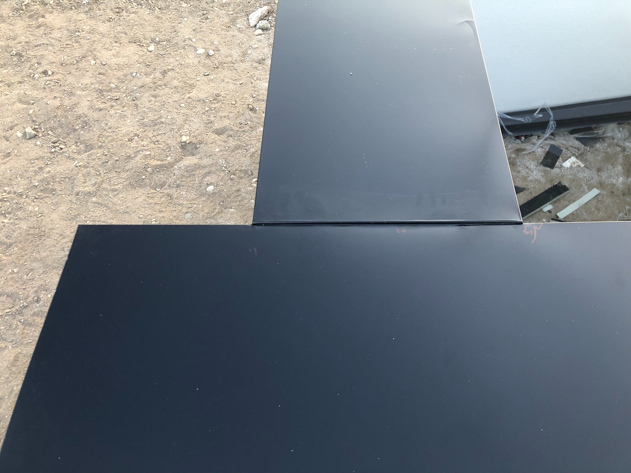 Szczegółowe ujęcie fragmentu dachu z blachy na placu budowy, widoczne połączenie arkuszy blachy i podłoże z piasku oraz resztki materiałów budowlanych.