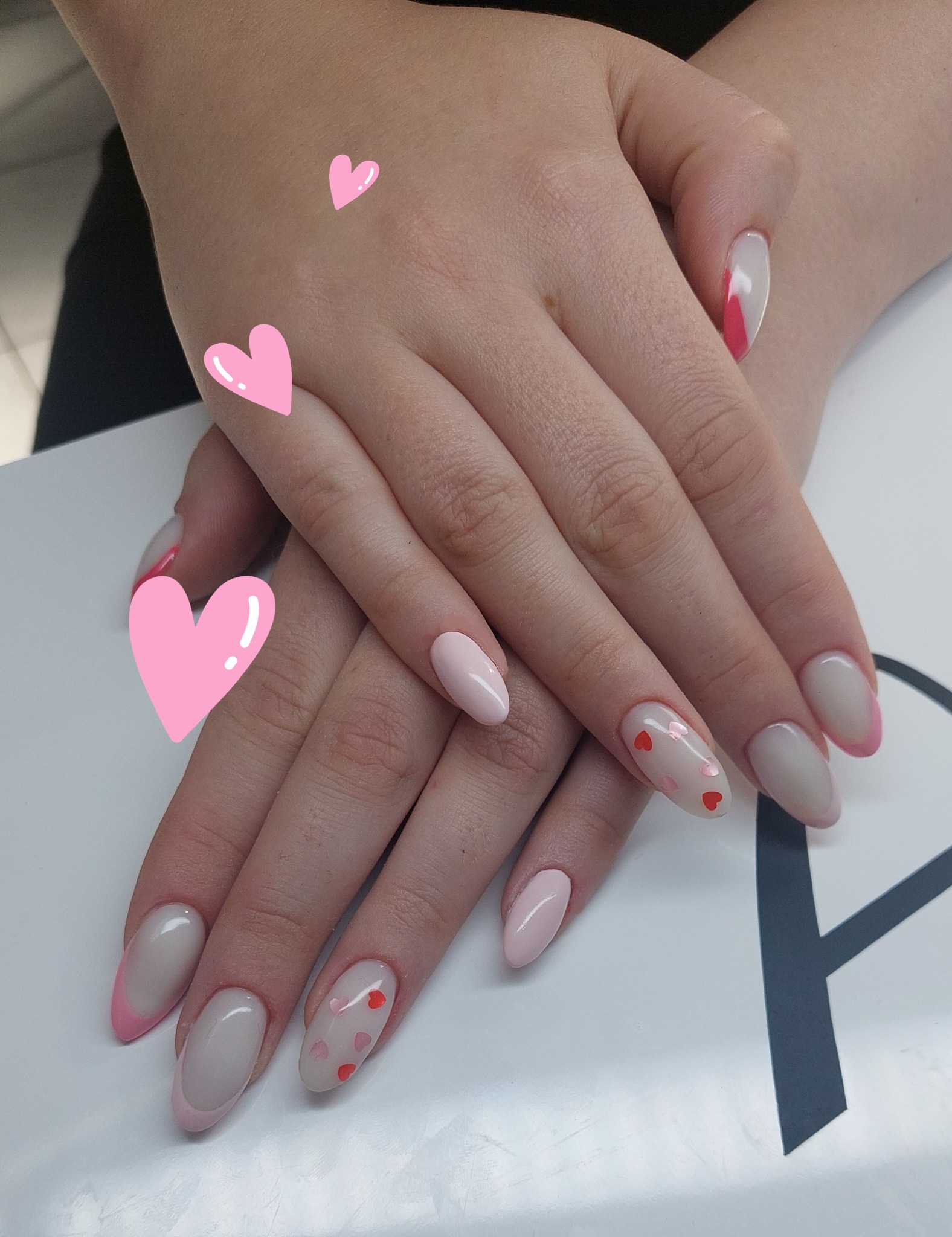 Dłonie z delikatnym, pastelowym manicure hybrydowym: french z różową końcówką i wzorem w serduszka. Romantyczny, kobiecy styl na białym tle.
