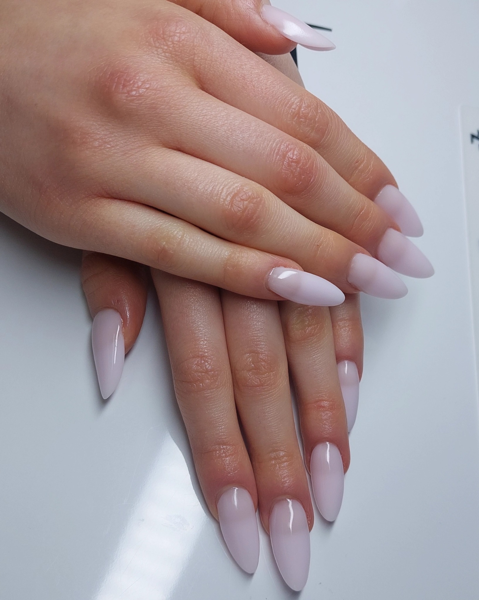 Dłonie z delikatnym, jasnoróżowym manicure hybrydowym o kształcie migdała. Czyste, zadbane skórki i błyszcząca powierzchnia lakieru. Minimalistyczny i elegancki wygląd.