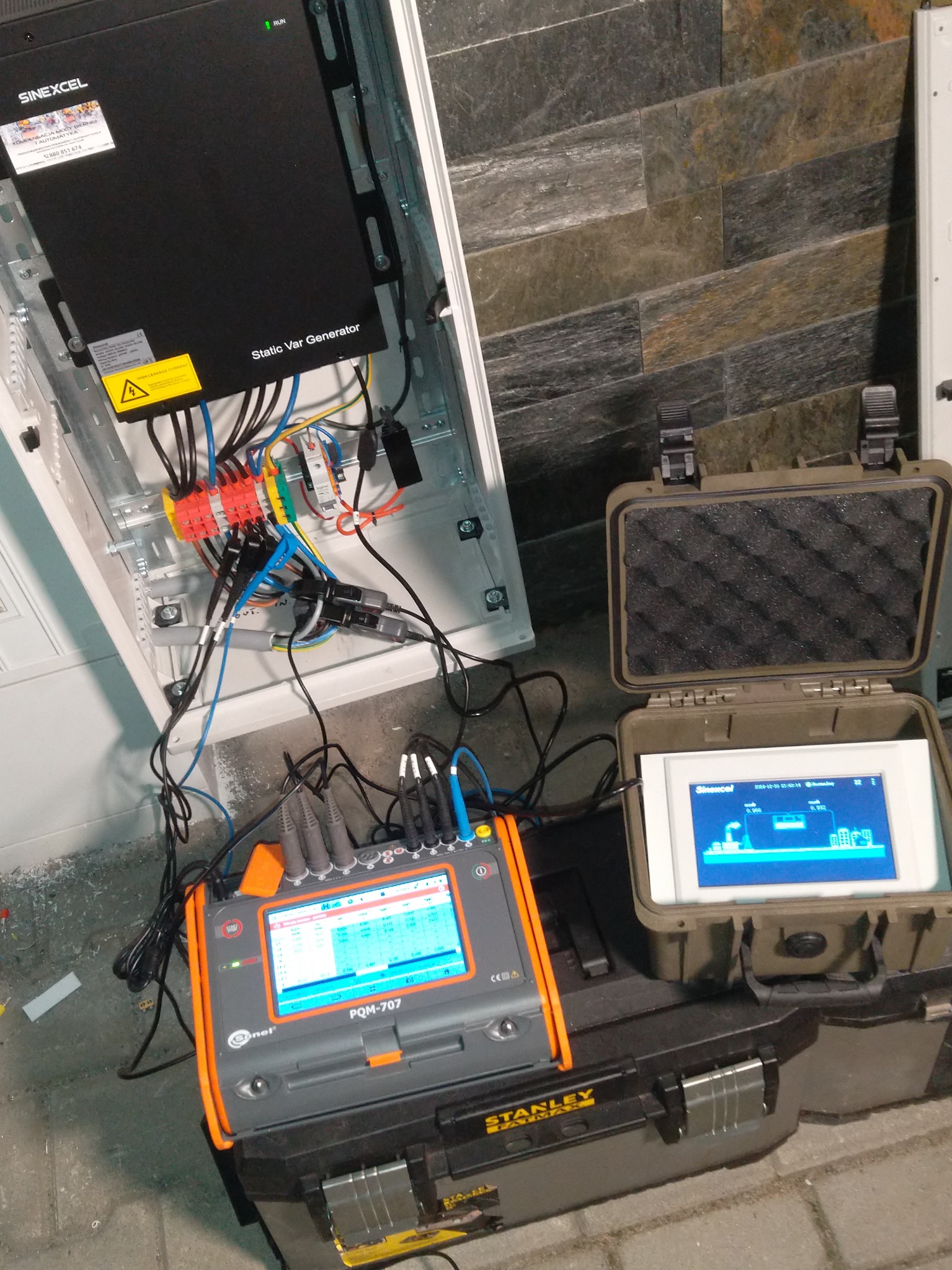 Podłączenie miernika PQM-707 marki Sonel do rozdzielnicy Sinexcel Static Var Generator w celu diagnostyki instalacji, widoczny ekran miernika oraz otwarty kufer z dodatkowym wyświetlaczem.