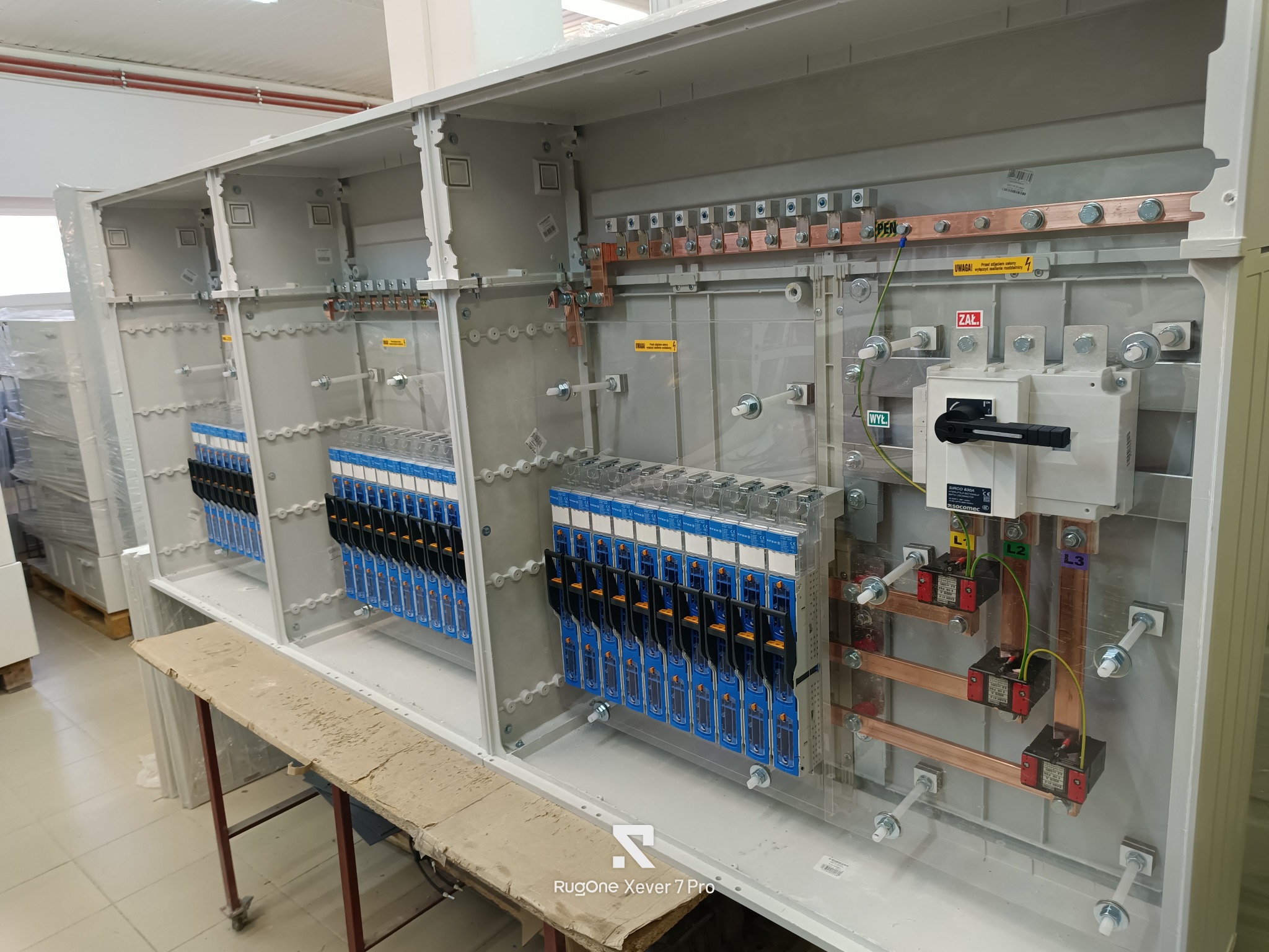 Rozdzielnica elektryczna w trakcie montażu, widoczne zabezpieczenia, szyny miedziane i okablowanie. Elementy zamontowane wewnątrz obudowy, widok z bliska.