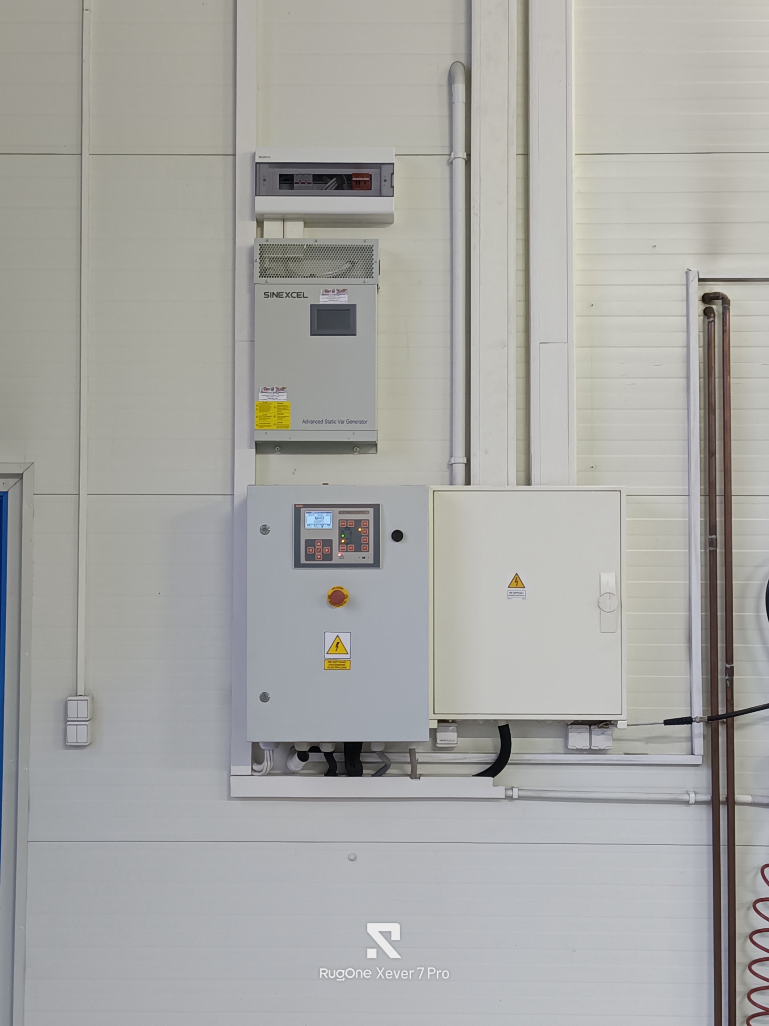 Zamontowana szafa sterownicza SINEEXCEL z panelem kontrolnym i wyłącznikiem awaryjnym na białej ścianie z blachy trapezowej. Widoczne przewody i rury instalacyjne.