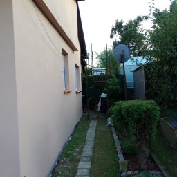 Bizoń Rafał usługi remontowo budowlane - Świeżo pomalowana elewacja domu w Sułkowicach, widoczne zabezpieczone okna i ścieżka z kostki prowadząca wzdłuż budynku.