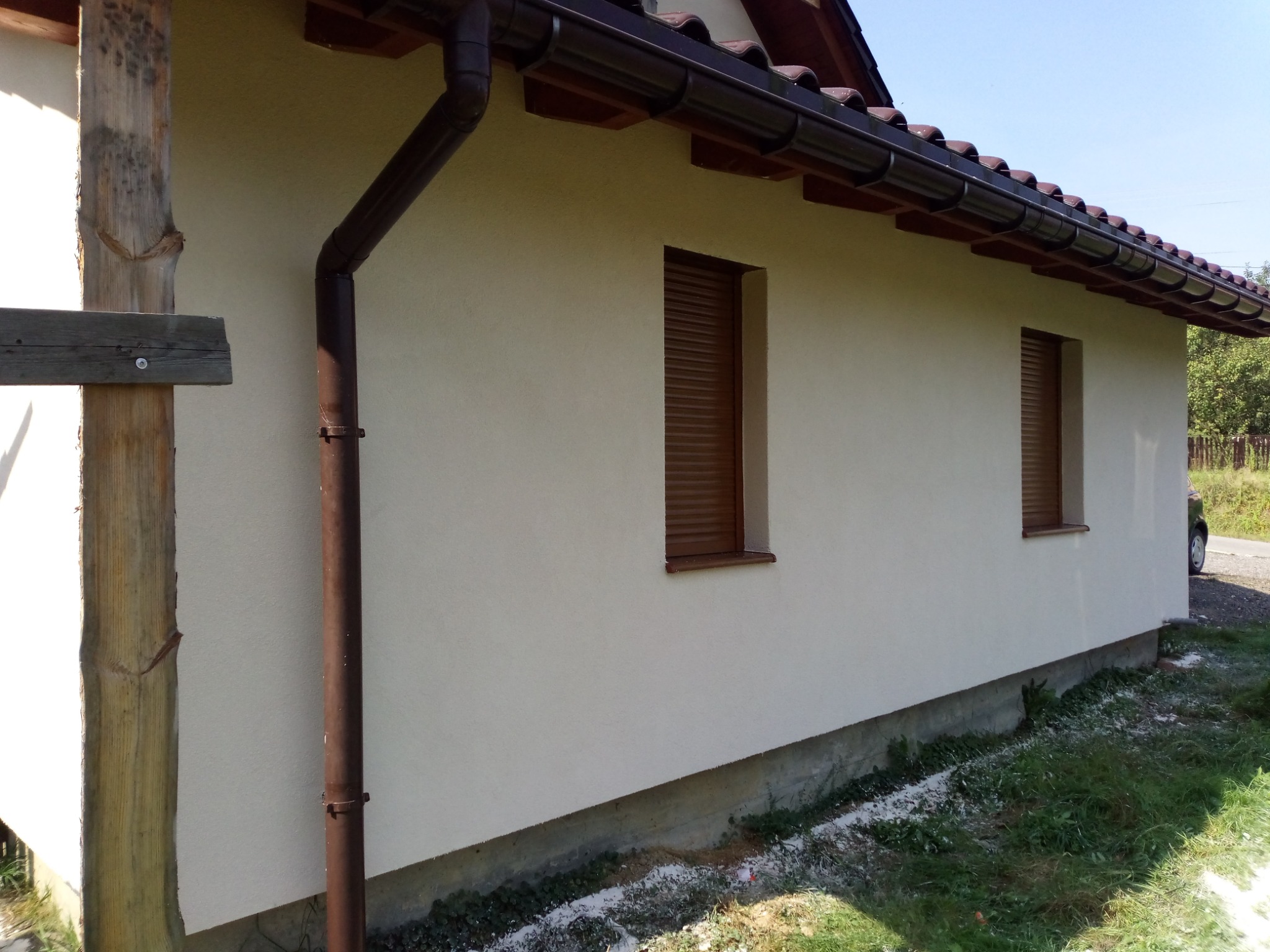 Ocieplony budynek z kremową elewacją, brązowymi rynnami i roletami okiennymi, widoczne ślady ocieplenia na gruncie.