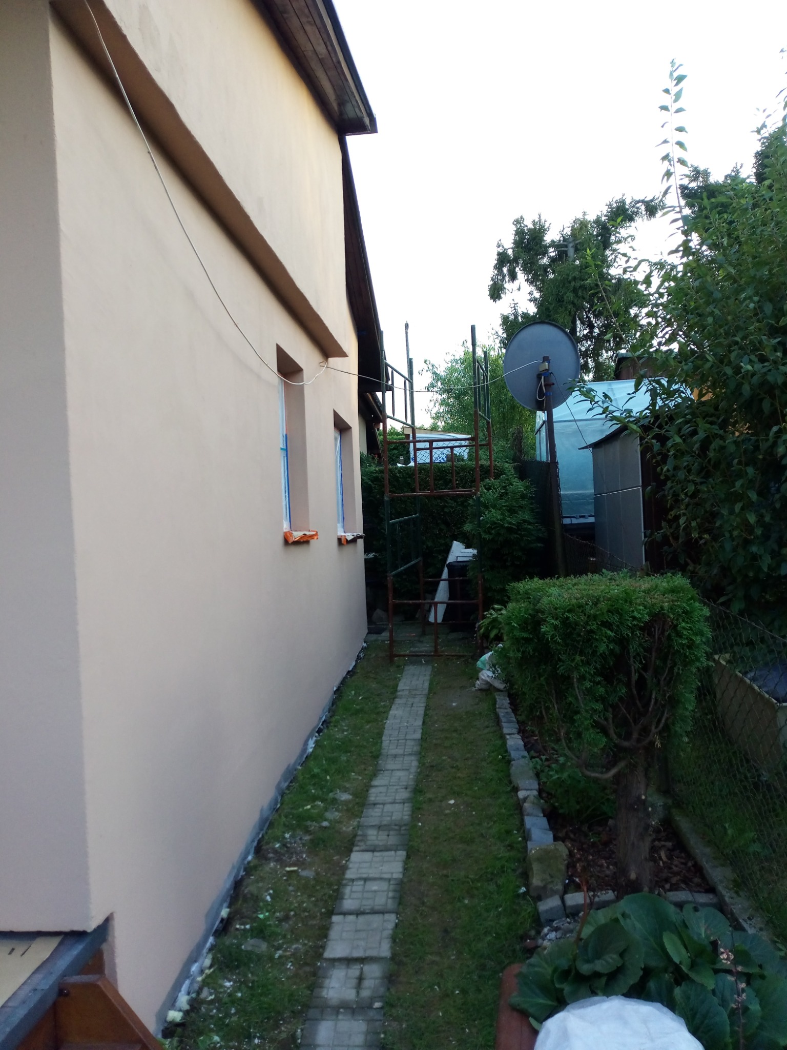 Świeżo pomalowana elewacja domu w Sułkowicach, widoczne zabezpieczone okna i ścieżka z kostki prowadząca wzdłuż budynku.