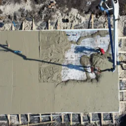 Zalewanie betonem zbrojonej płyty fundamentowej pod budynek, widok z drona, beton częściowo wylany, widoczni pracownicy i pompa do betonu.