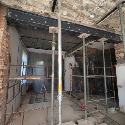 New Structure - Wnętrze w trakcie remontu z podpartym stropem belkami stalowymi, widoczne rusztowania i zabezpieczenia folią.