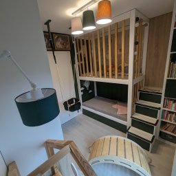New Structure - Pokój dziecięcy z łóżkiem piętrowym z drewnianą barierką, huśtawką na linie, lampą podłogową z zielonym abażurem i drewnianymi zabawkami.