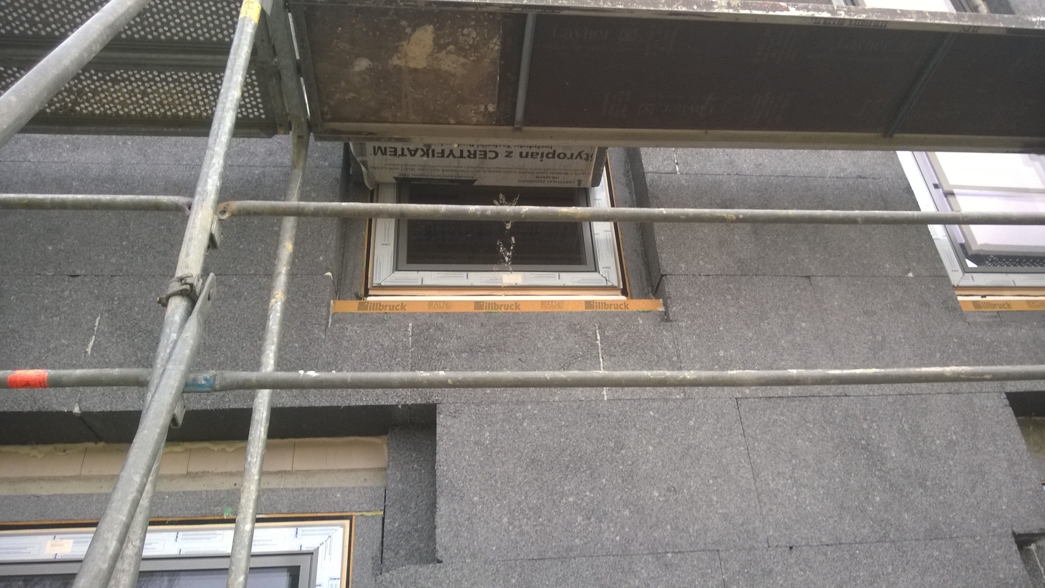 Montaż okna w ocieplonej ścianie budynku, widoczne rusztowanie i taśma uszczelniająca Illbruck