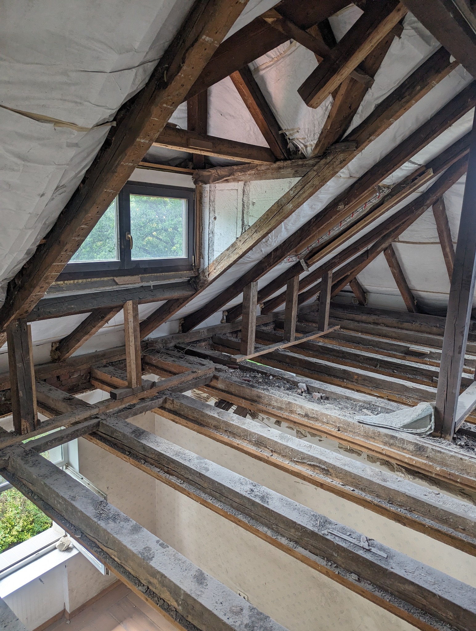 Demontaż drewnianej konstrukcji dachu z widoczną izolacją, elementami więźby i oknem dachowym, w trakcie remontu poddasza.