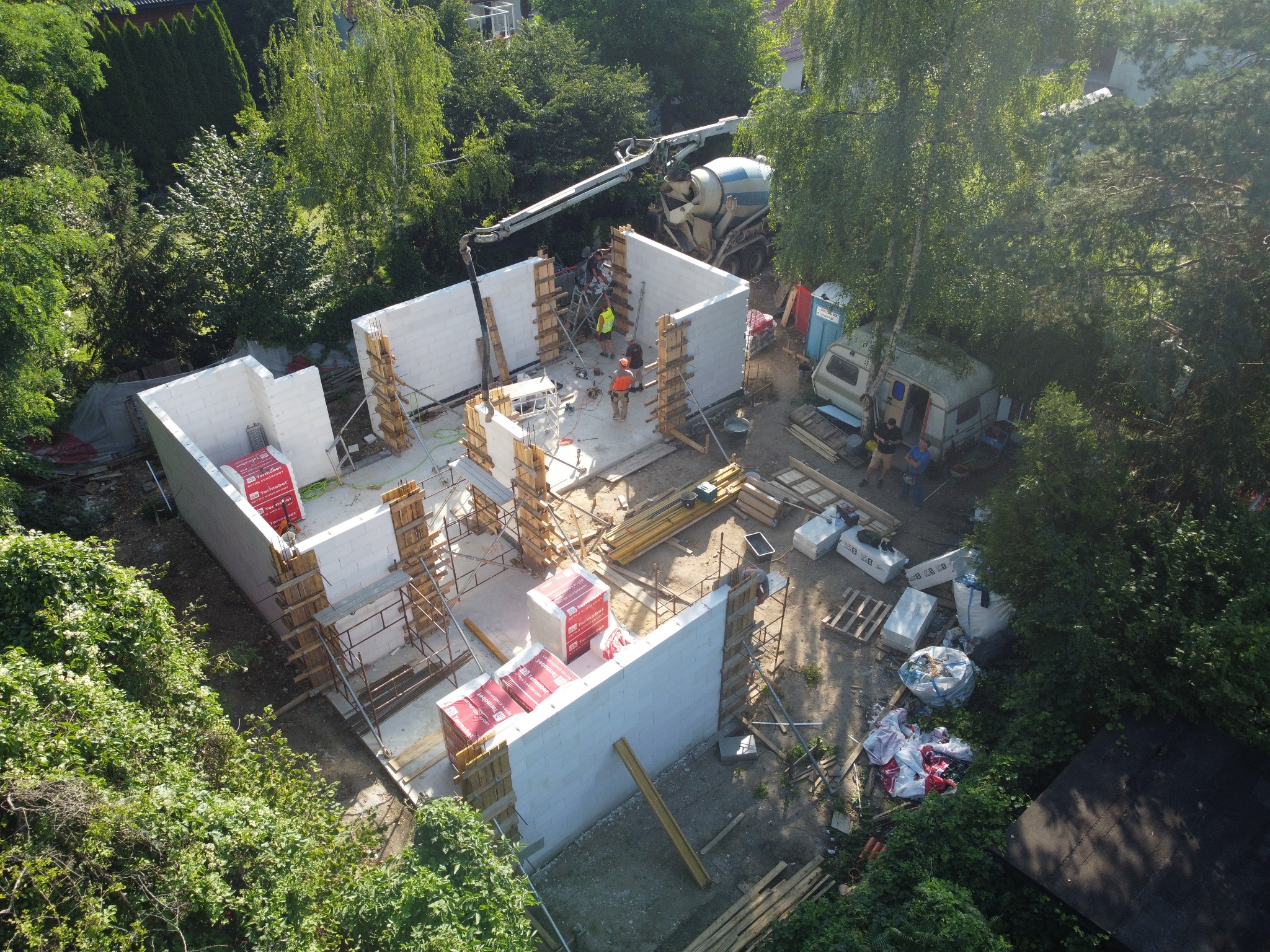 Budowa domu z betonu komórkowego: widok z góry na wznoszone ściany, szalunki i betoniarkę na działce z bujną zielenią.